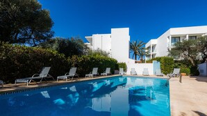 A swimming pool with lounge chairs, surrounded by greenery and modern buildings. - Apartment 'Apartamento Bon Aire N1' with Shared Pool, Wi-Fi and Air Conditioning (Cala Ferrera)