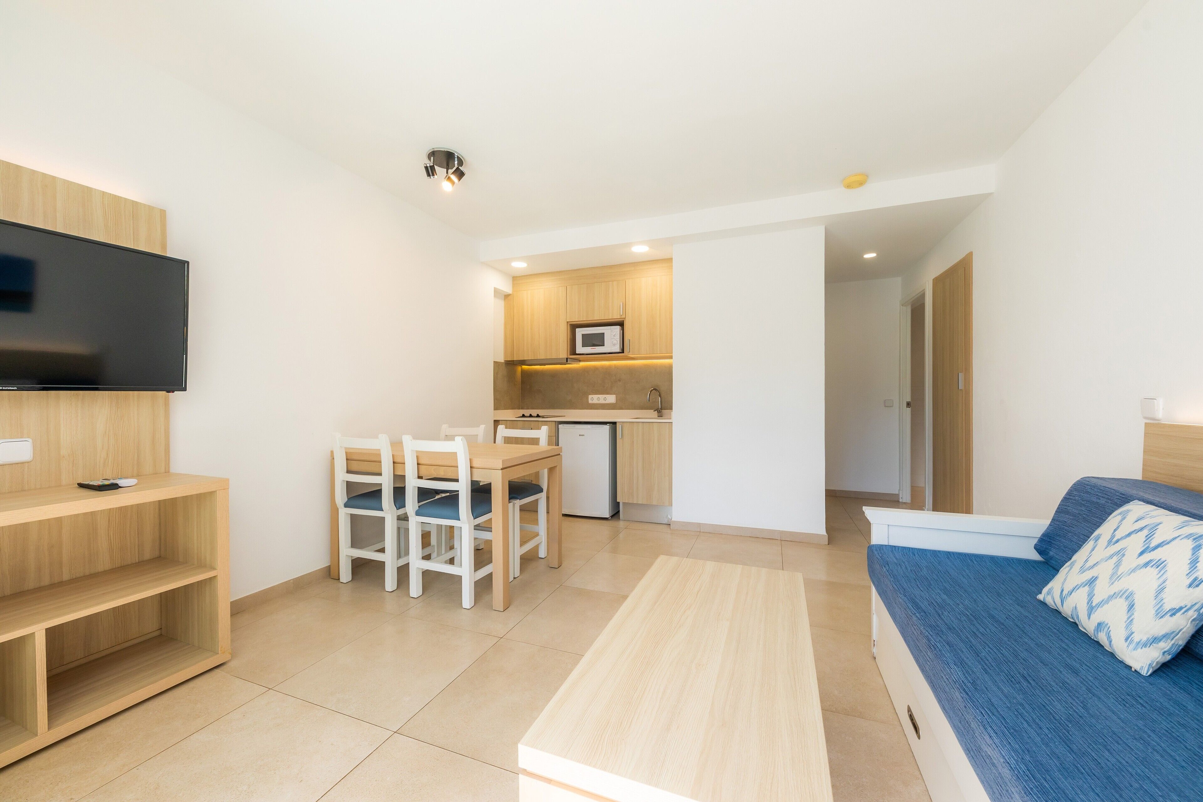 Una habitación moderna con televisor, una mesa de comedor con sillas, kitchenette y una cama.