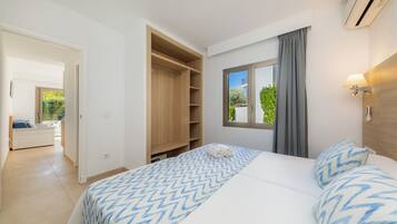 Un dormitorio con cama, vestidor, ventana con cortinas y vistas al exterior.