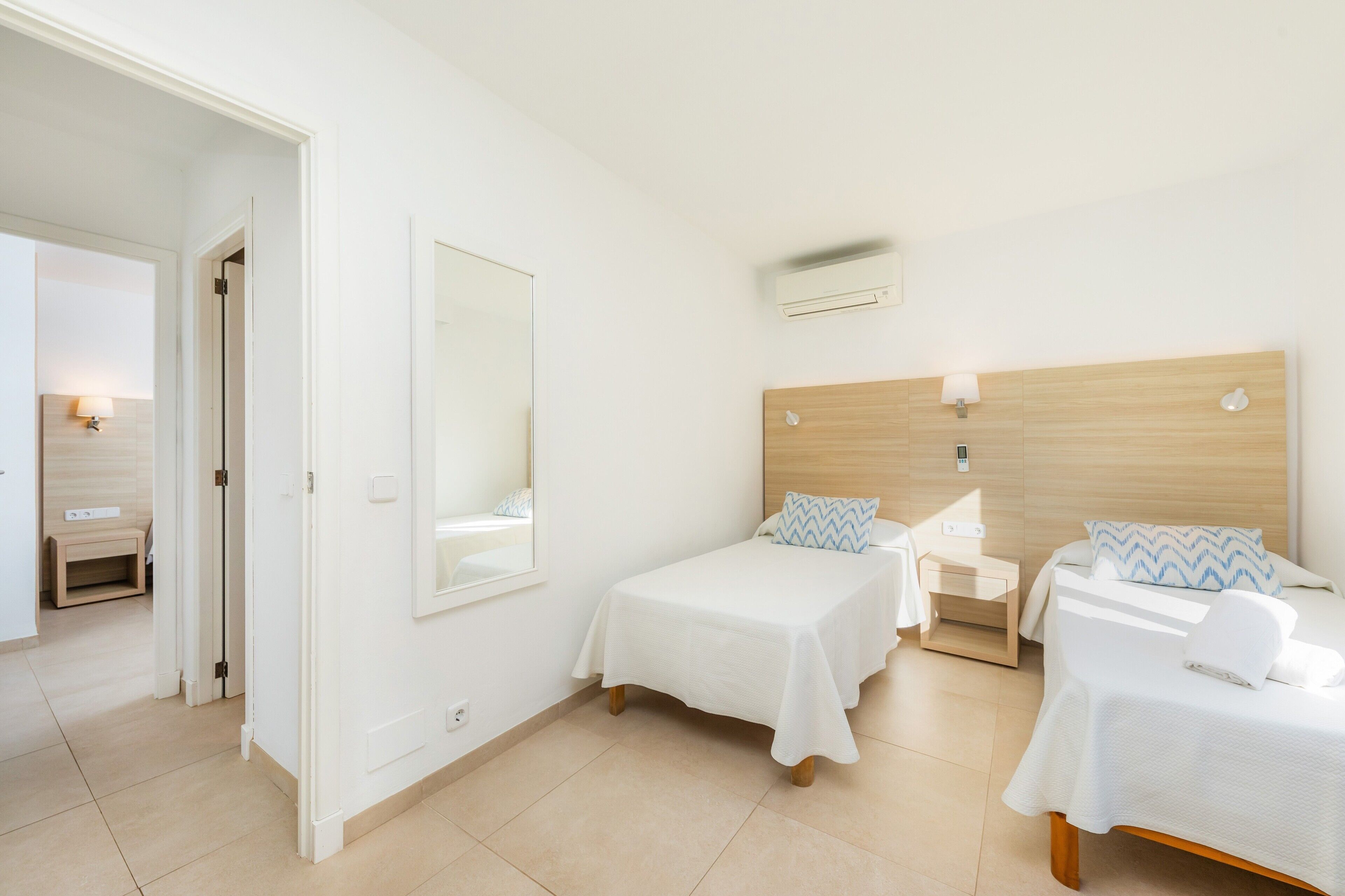 Une chambre d’hôtel avec deux lits, un miroir, une table de chevet avec une lampe et un climatiseur fixé au mur.
