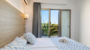 A hotel room with a bed, a nightstand, a lamp, a window with curtains, and a view of palm trees. - Apartment 'Aquamarina 5' with Shared Pool, Wi-Fi, and Air Conditioning (Cala Ferrere)