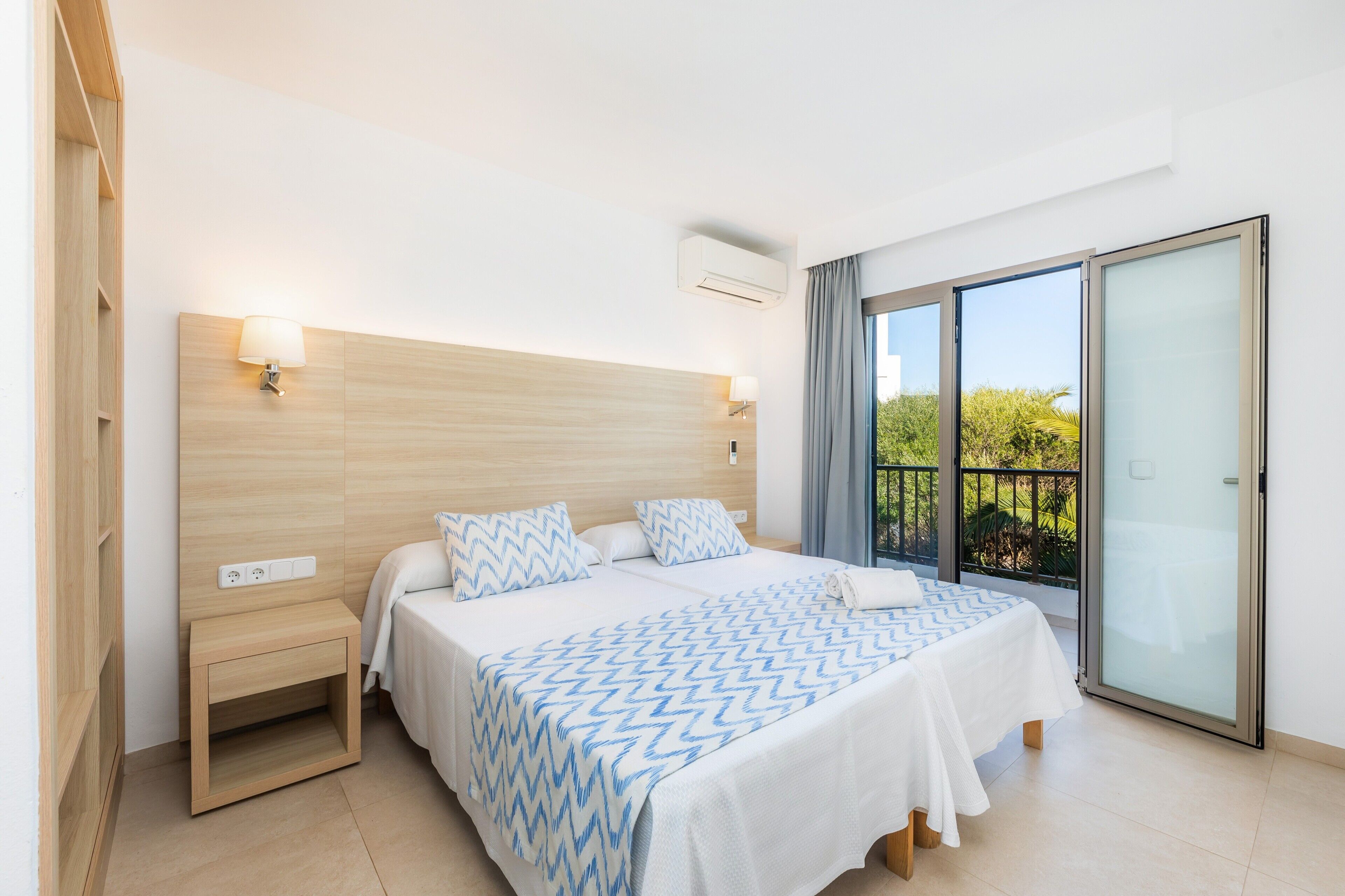 Habitación de hotel con cama, mesitas de noche, ventana con vistas y un equipo de aire acondicionado.