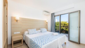 A hotel room with a bed, bedside tables, a window with a view, and an air conditioning unit. - Apartment 'Aquamarina 7' with Shared Pool, Wi-Fi and Air Conditioning (Cala Ferrera)