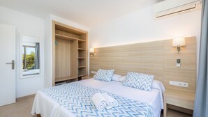 A hotel room with a bed, a wardrobe, a bedside table, a lamp, and an air conditioning unit. - Apartment 'Aquamarina 7' with Shared Pool, Wi-Fi and Air Conditioning (Cala Ferrera)
