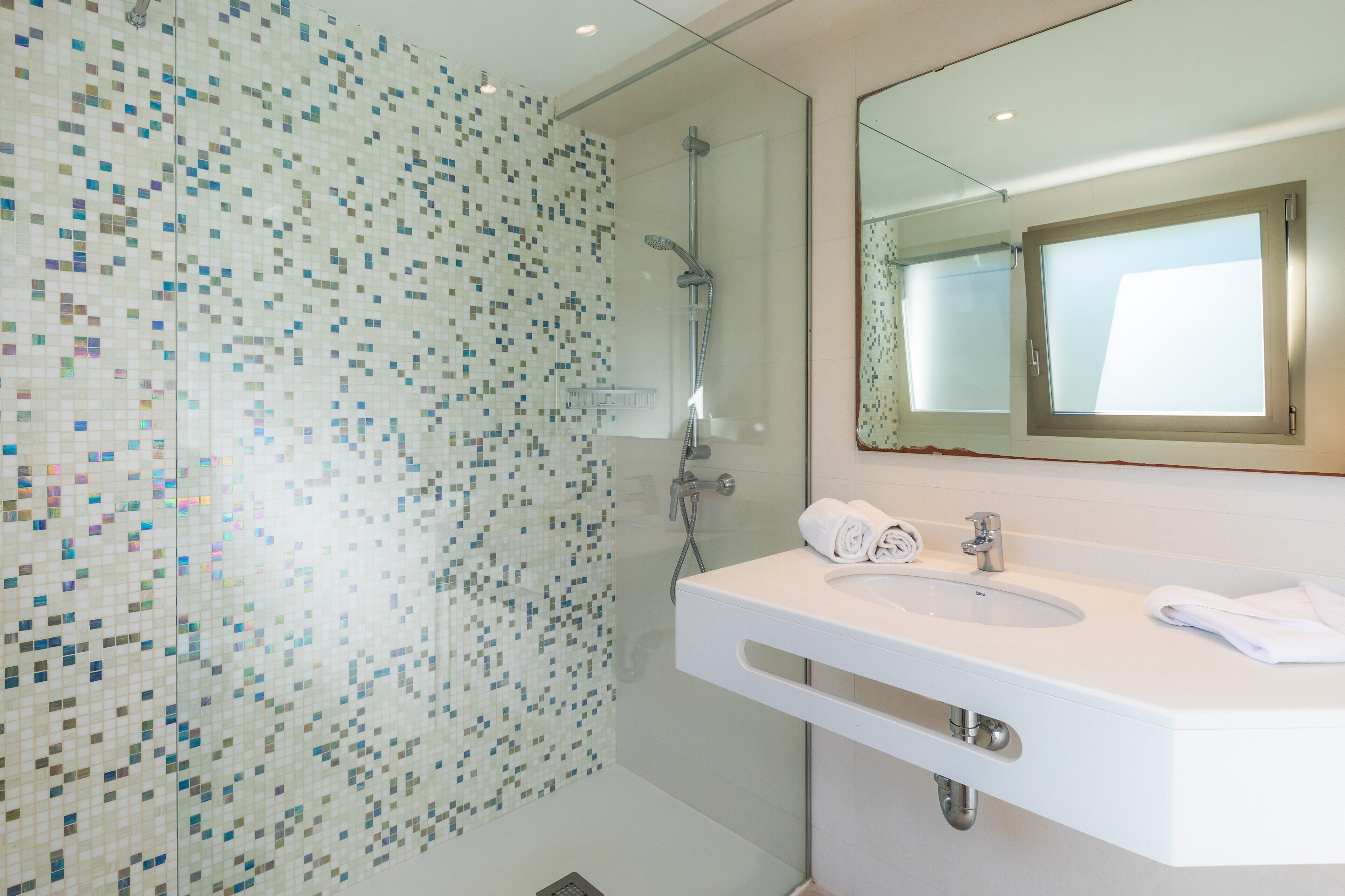 A modern bathroom with a mosaic shower wall, a white sink, and a large mirror.