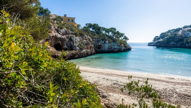 A coastal landscape with a beach, rocky cliffs, and a building on a hill. - Apartment 'Aquamarina 7' with Shared Pool, Wi-Fi and Air Conditioning (Cala Ferrera)