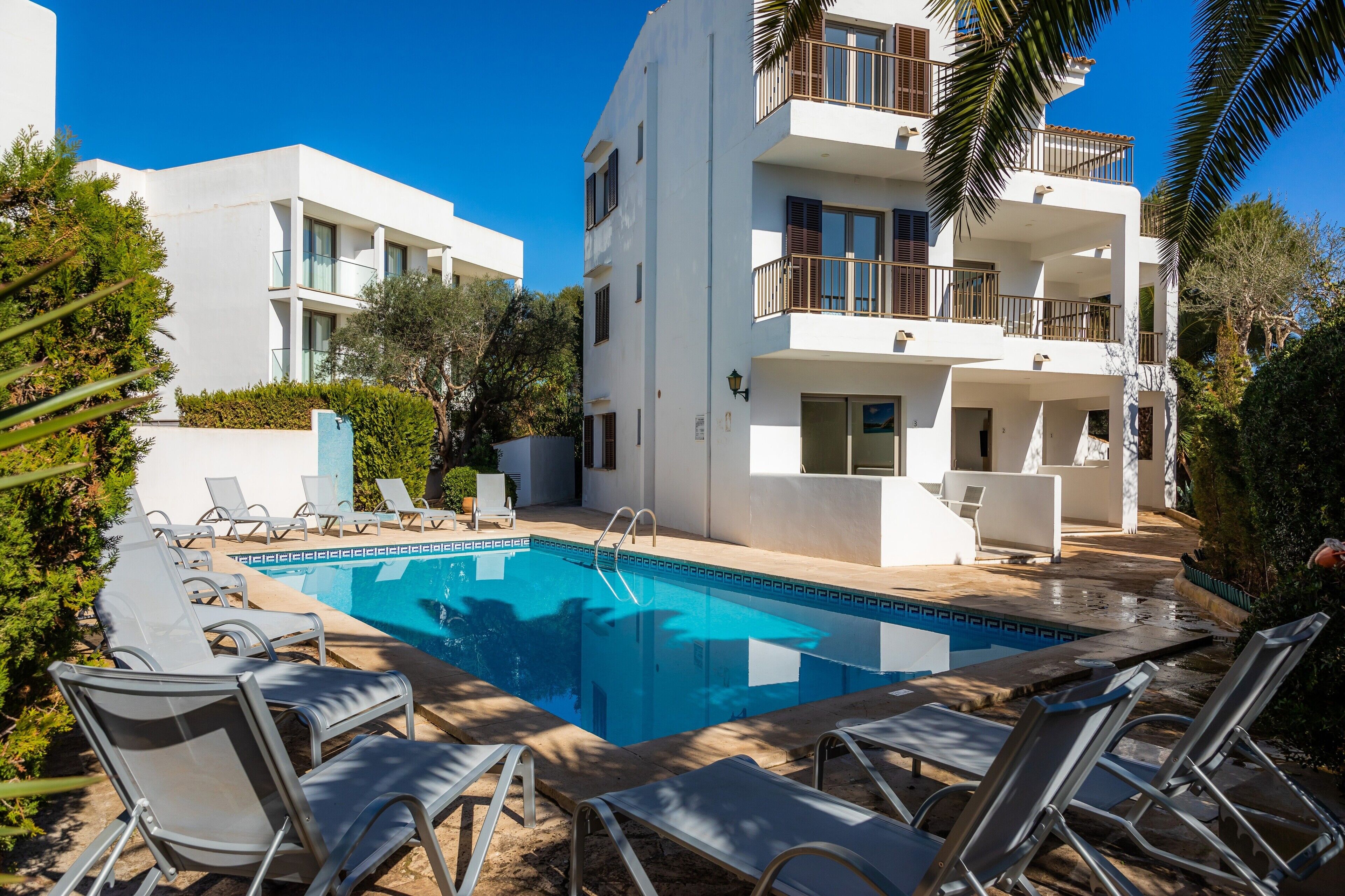 A modern building with a pool, lounge chairs, and a clear blue sky.