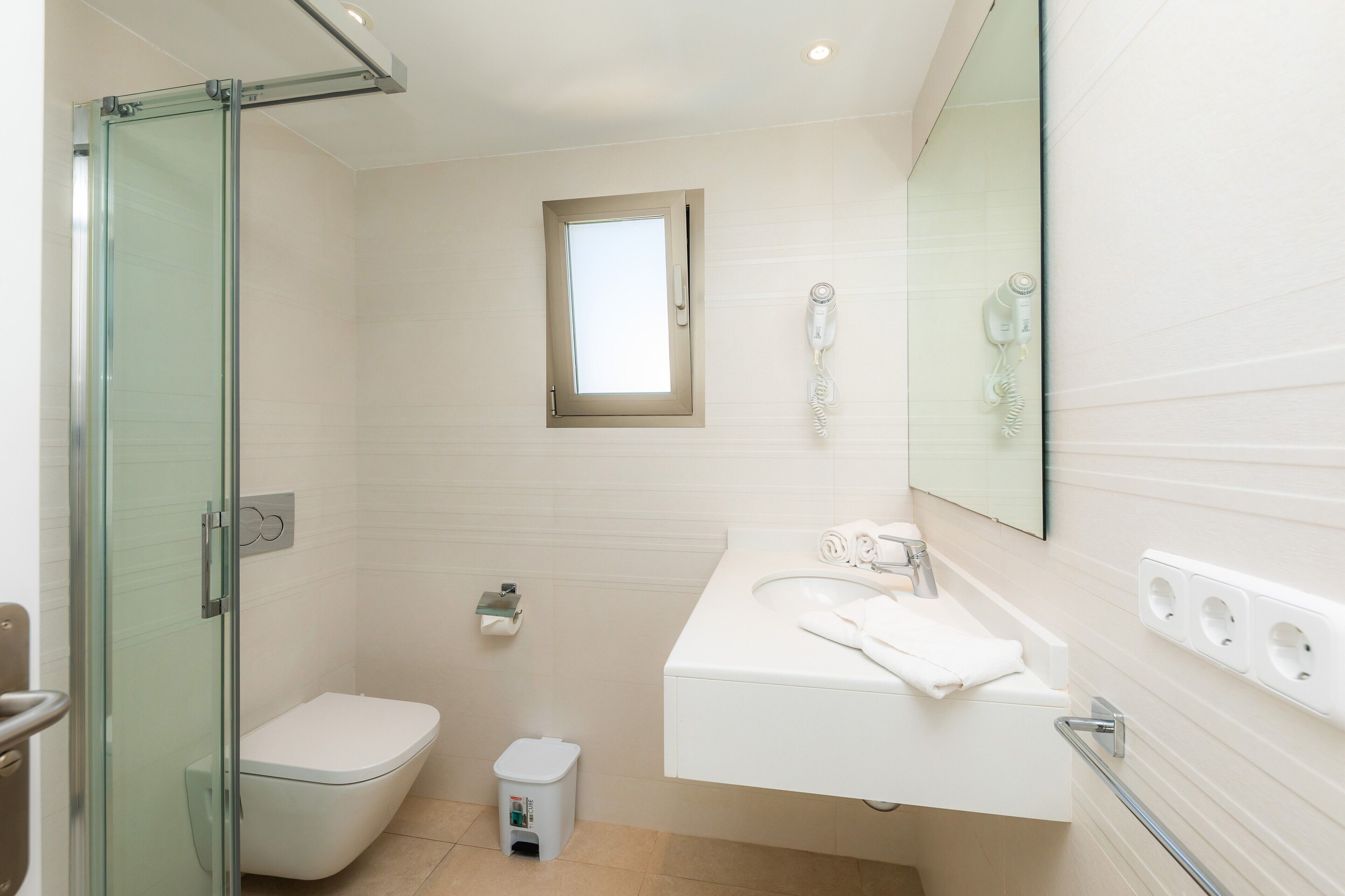 A modern bathroom with a glass shower enclosure, a toilet, a sink with a towel, and a mirror.