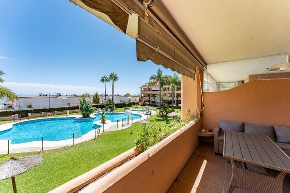 A balcony with a view of a swimming pool, a lounge area, and a building in the background.
