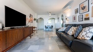 Een moderne woonkamer met een flatscreen-tv, een houten kast, een leren bank en een eethoek op de achtergrond.