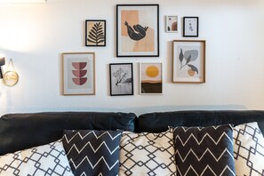 A room with a bed, a wall with framed artwork, and a lamp.