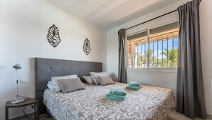 Een slaapkamer met een bed, kussens, een nachtkastje, een lamp en een raam met gordijnen.