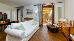A living room with a white sofa, a wooden coffee table, a dining table with chairs, a bookshelf, and a view through an open door to an outdoor patio. - Apartment 'In The Center Of Salò' with Balcony, Wi-Fi and Air Conditioning (Salò)