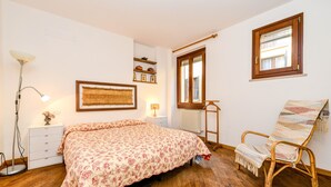 A bedroom with a bed, bedside lamp, wooden floor, window, and a chair with a blanket. - Apartment 'In The Center Of Salò' with Balcony, Wi-Fi and Air Conditioning (Salò)