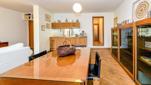 A dining area with a glass table, wooden chairs, a woven bag, and a kitchen in the background. - Apartment 'In The Center Of Salò' with Balcony, Wi-Fi and Air Conditioning (Salò)