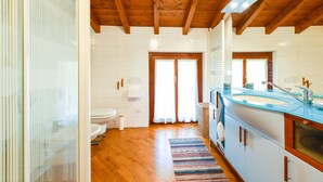 A bathroom with a wooden ceiling, white tiles, a toilet, a sink with a blue countertop, and a striped rug. - Apartment 'Attic In The Center Of Salò' with Balcony, Wi-Fi and Air Conditioning (Salò)