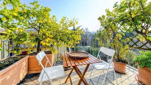 A balcony with a wooden table, chairs, potted plants, and a view of the surrounding area. - Apartment 'Attic In The Center Of Salò' with Balcony, Wi-Fi and Air Conditioning (Salò)