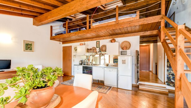 A spacious loft-style room with a wooden ceiling, a kitchen area, and a dining table with a potted plant. - Apartment 'Attic In The Center Of Salò' with Balcony, Wi-Fi and Air Conditioning (Salò)