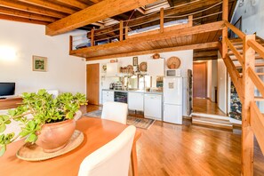 Un vaste espace de vie de style loft, doté d’un plafond en bois, d’un coin cuisine et d’une table à manger agrémentée d’une plante en pot.