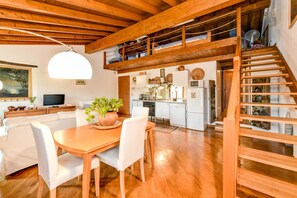 Une cuisine spacieuse avec des meubles en bois, un coin repas avec une table et des chaises en bois, et une chambre à l’étage avec un escalier en bois.