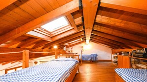 An attic bedroom with wooden beams, a skylight, two beds with checkered bedding, a desk, and a bookshelf. - Apartment 'Attic In The Center Of Salò' with Balcony, Wi-Fi and Air Conditioning (Salò)