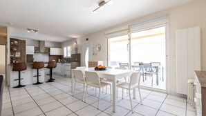 Een moderne keuken met witte kasten, een eettafel met stoelen, en een grote schuifpui naar buiten.