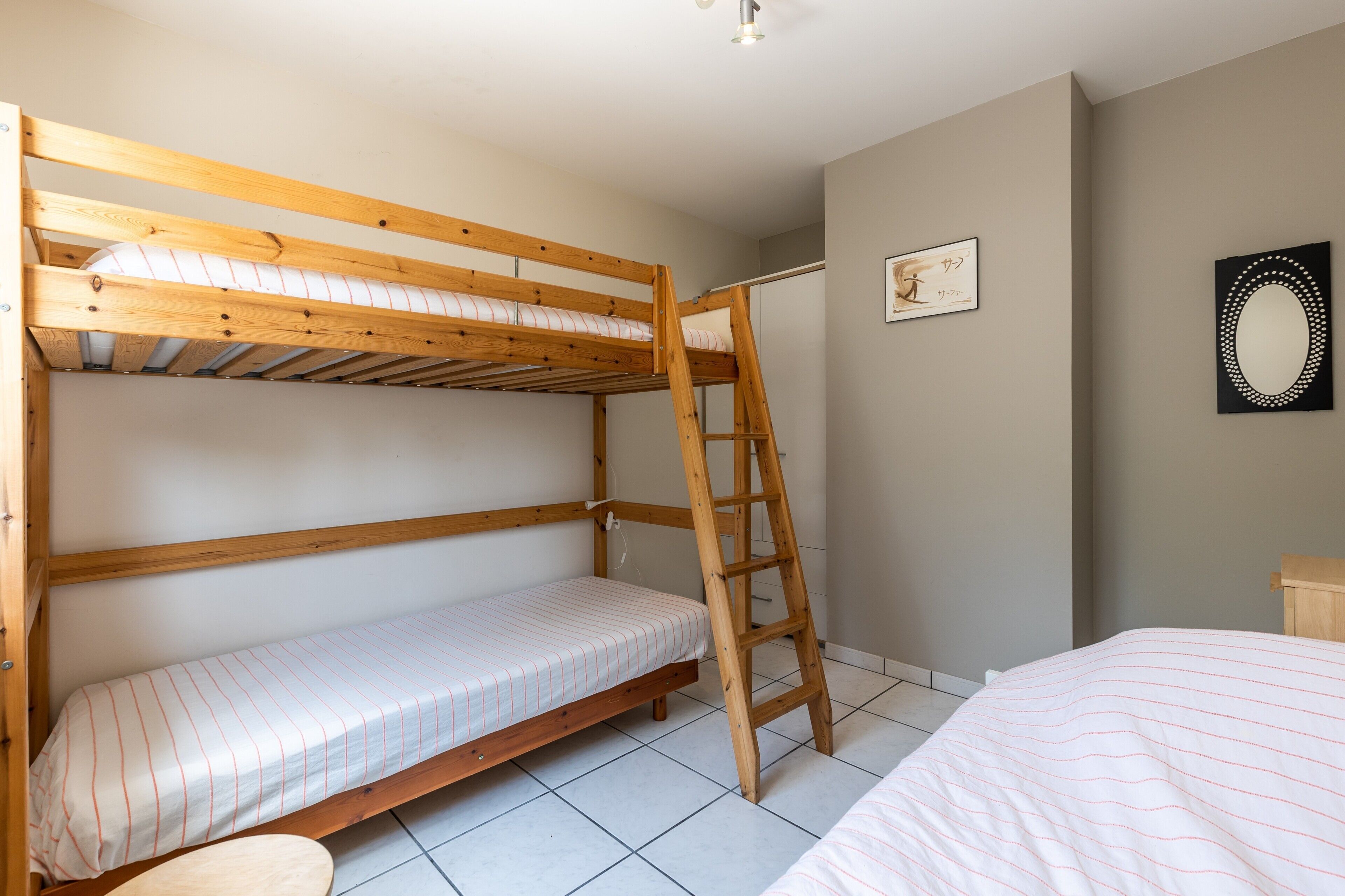 A bunk bed room with a ladder, a small bedside table, and a framed picture on the wall.