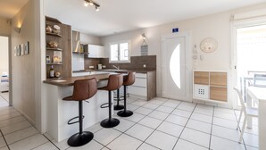 Een moderne keuken met een centraal eiland, barstoelen en een eethoek met een witte tafel.