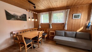 Un interno in legno con un tavolo da pranzo, sedie, un divano e due finestre con tende.