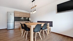 A modern kitchen with a built-in refrigerator, wooden cabinets, a dining table with chairs, and a flat-screen TV mounted on the wall.