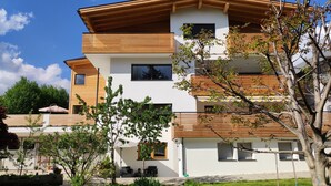 A modern multi-story residential building with a flat roof, large windows, and wooden accents.