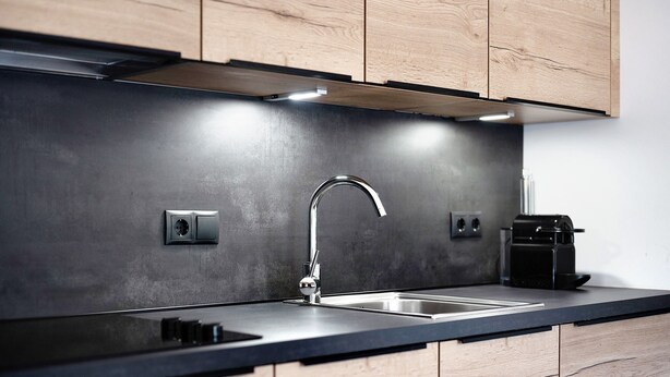 A modern kitchen with a stainless steel sink, wooden cabinets, and a black countertop.