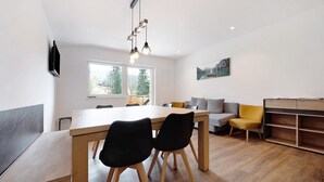 A modern living space with a wooden dining table, black chairs, a sofa, and a built-in bookshelf.