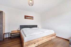 A bedroom with a wooden bed frame, a nightstand, a desk, and a chair.