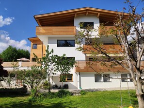 A modern multi-story residential building with a flat roof, large windows, and a well-maintained lawn.