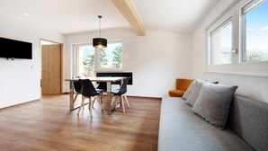 A modern living room with a sofa, a dining area with a table and chairs, and a kitchen area with a window. - Holiday Apartment "Haus Mader 1" with Mountain View, Private Terrace & Wi-Fi (Riscone Brunico)