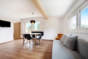 A modern living room with a sofa, a dining area with a table and chairs, and a kitchen area with a window.
