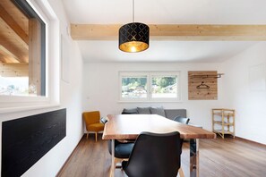 A modern dining area with a wooden table and chairs, a hanging pendant light, and a view of the outdoors.
