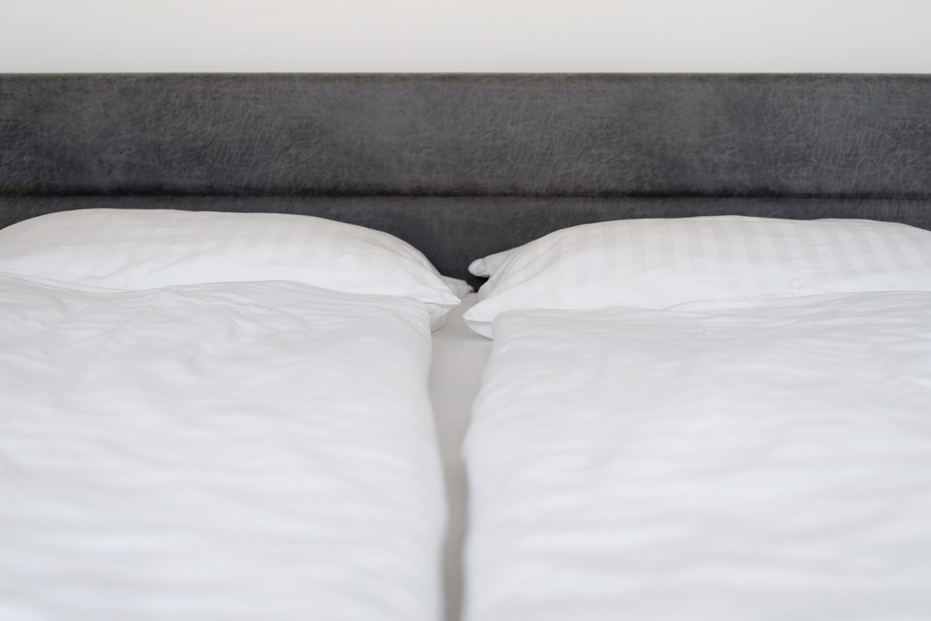 Ein Bett mit weißer Bettwäsche und einem grauen Kopfteil.