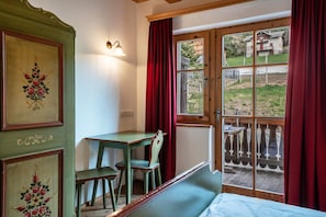 Une pièce avec une table en bois, deux chaises, un banc, une fenêtre avec des rideaux et une porte donnant sur l’extérieur.
