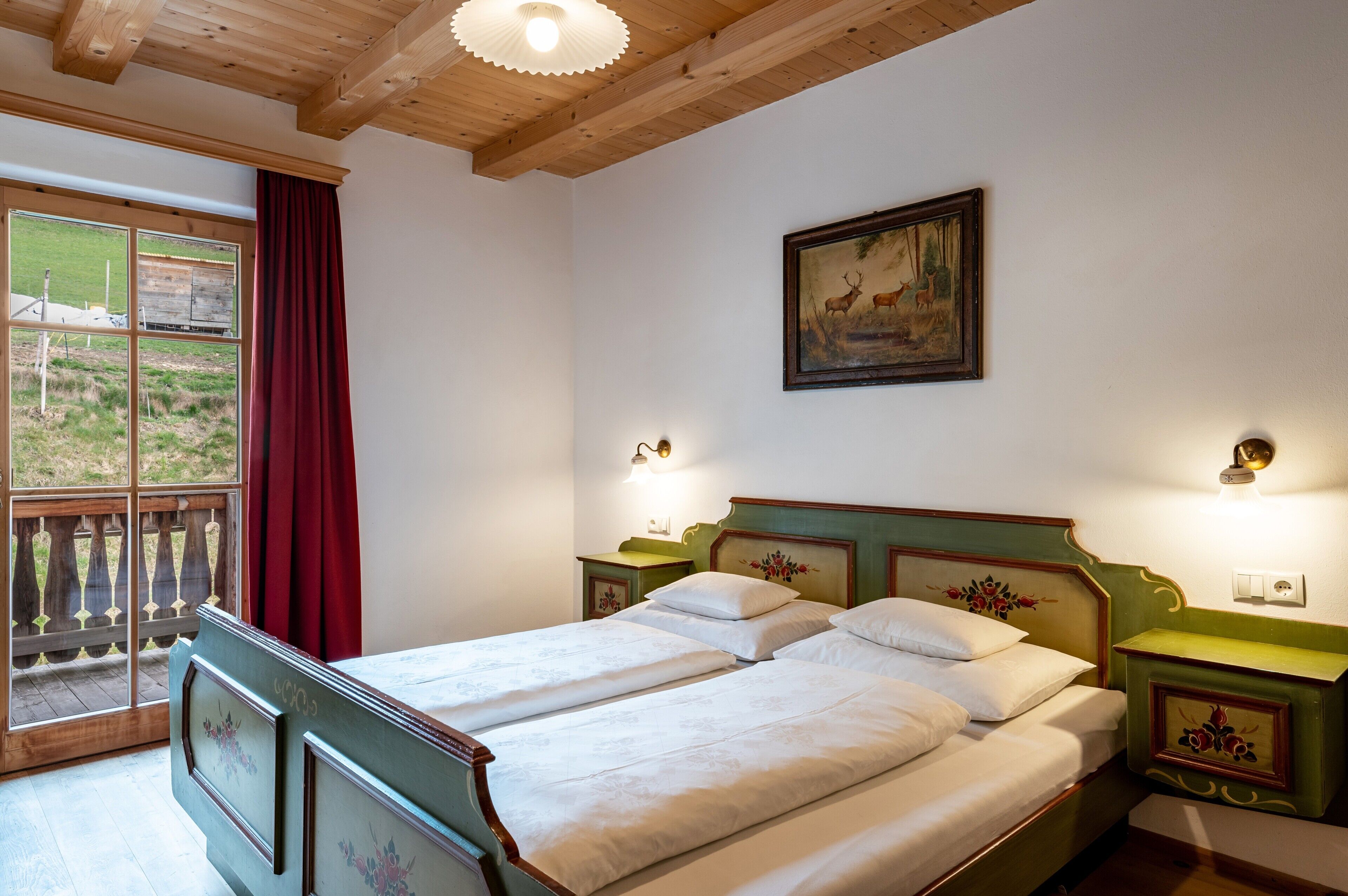Une pièce avec un lit, une fenêtre donnant sur un beau paysage, un tableau au mur et un plafond en bois.