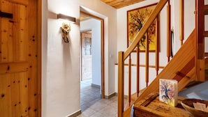 Un escalier en bois orné d’un tableau, une porte en bois et un couloir menant à une autre pièce.