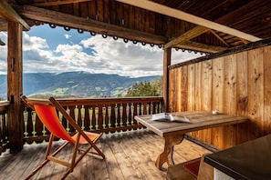 A wooden deck with a table and a chair, overlooking a mountainous landscape.