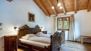 A wooden-framed bed with a headboard, a bedside table, a nightstand, a window with curtains, and a ceiling with exposed beams. - Apartment 'Biohof Maurer Apt Vogelstimmen' with Mountain View, Shared Garden and Wi-Fi (Laion)