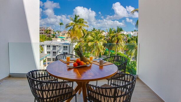 A balcony with a wooden table and chairs, a fruit bowl, and a glass of orange juice.