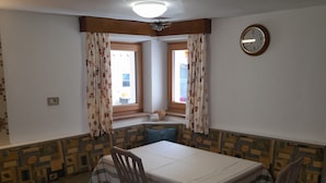 Un comedor con una mesa, sillas, un banco estampado y un reloj en la pared.