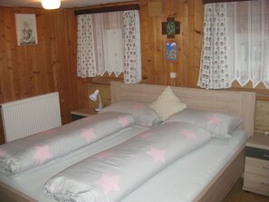 A wooden-paneled room with a bed, two nightstands, a lamp, and a radiator.
