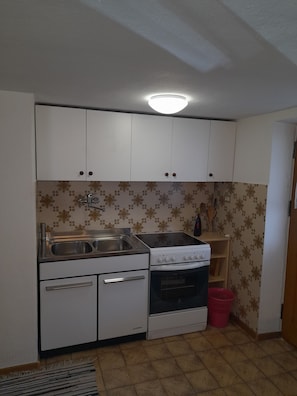 A compact kitchen with white cabinets, a double sink, a stove, and a small oven.