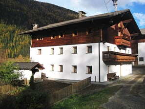 Un edificio a due piani con facciata bianca e sezione superiore in legno, caratterizzato da numerose finestre e un balcone.