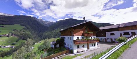 Un bâtiment à deux étages doté d’un balcon en bois, entouré d’un paysage rural avec des montagnes et de la verdure.